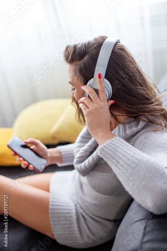 Young beautiful woman looking on play list on mobile phone and listen music over headphones