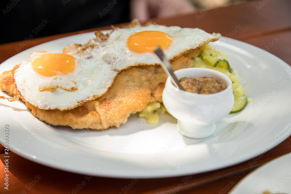 Schweine Fleisch Schnitzel Wiener Art mit Spiegelei als Hamburger dazu Gurken Kartoffelsalat und Bayrischen süßen Senf im Biergarten Restaurant