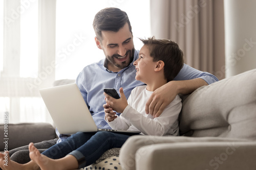 Happy dad and son relax on couch using gadgets