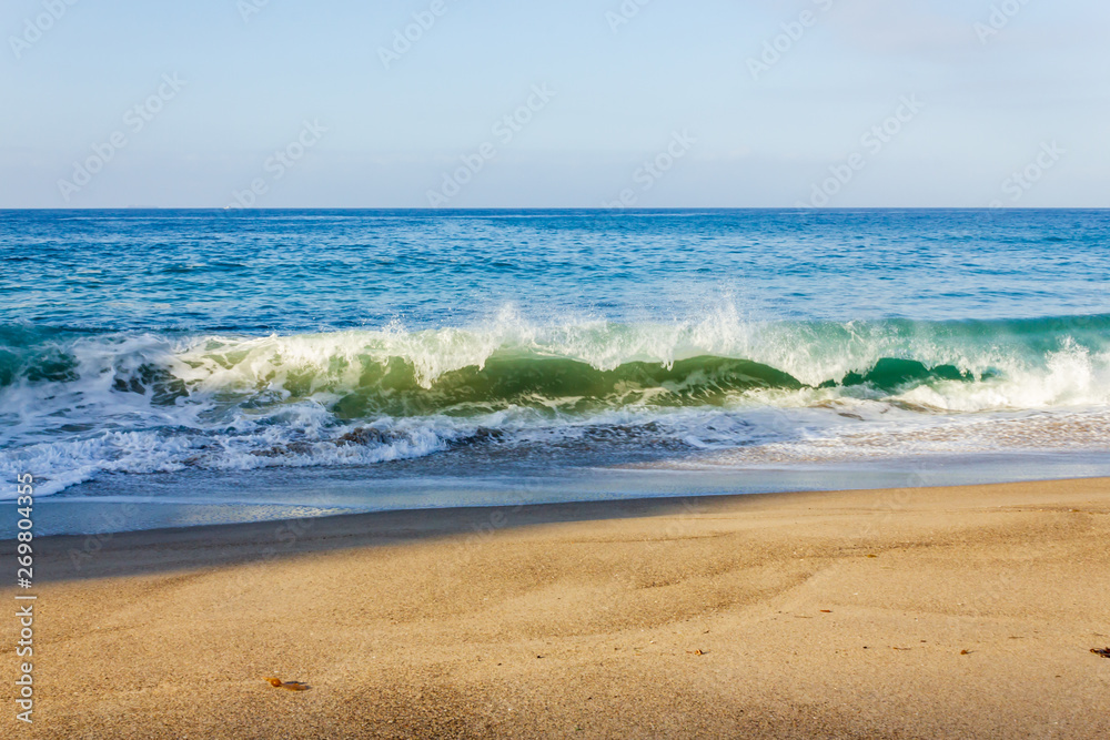 breaking wave on shoreline with backwash, backspray, with sandy beach