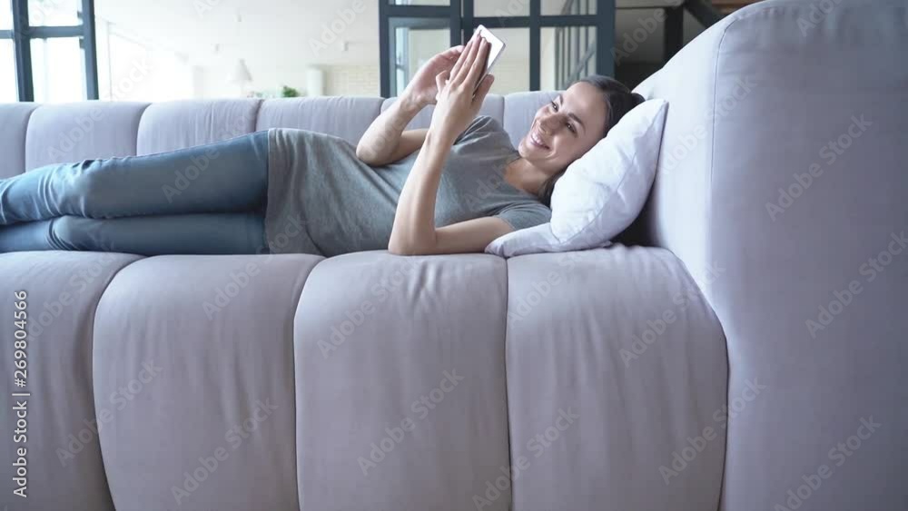 Yourself rest time. Happy cute young woman is using smart phone in hands while she lying on the couch at home. Yourself rest time. Happy cute young woman is using smart phone in hands while she lying on the couch at home.