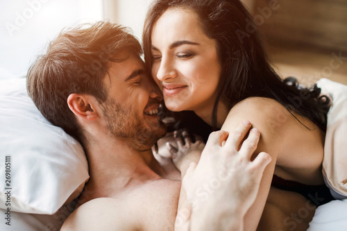 Young sexy couple have intimacy on bed. Beautiful picture of woman lying on man and smile. Spend time together in bed. Nice tender people. photo