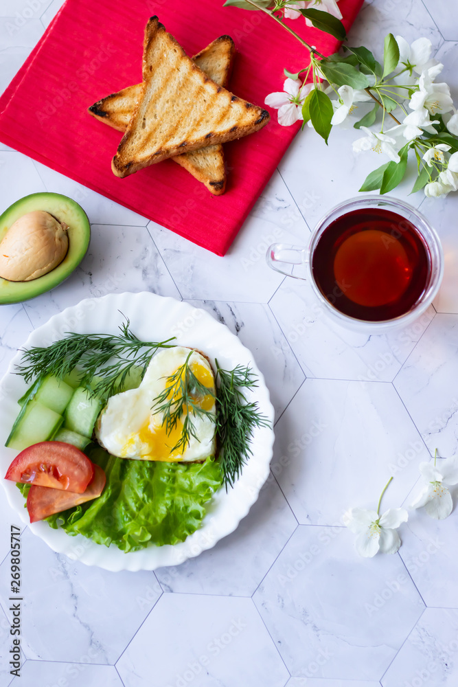 Fried eggs with lettuce, cucumber and tomato slices on a light background