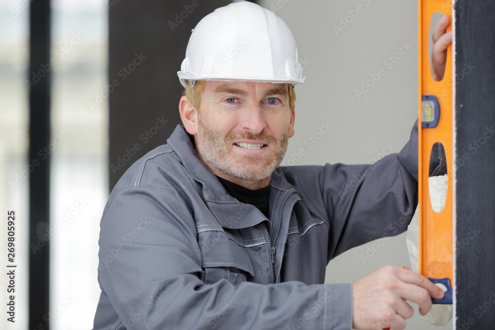 builder in helmet is measuring wall with level builder in helmet is measuring wall with level