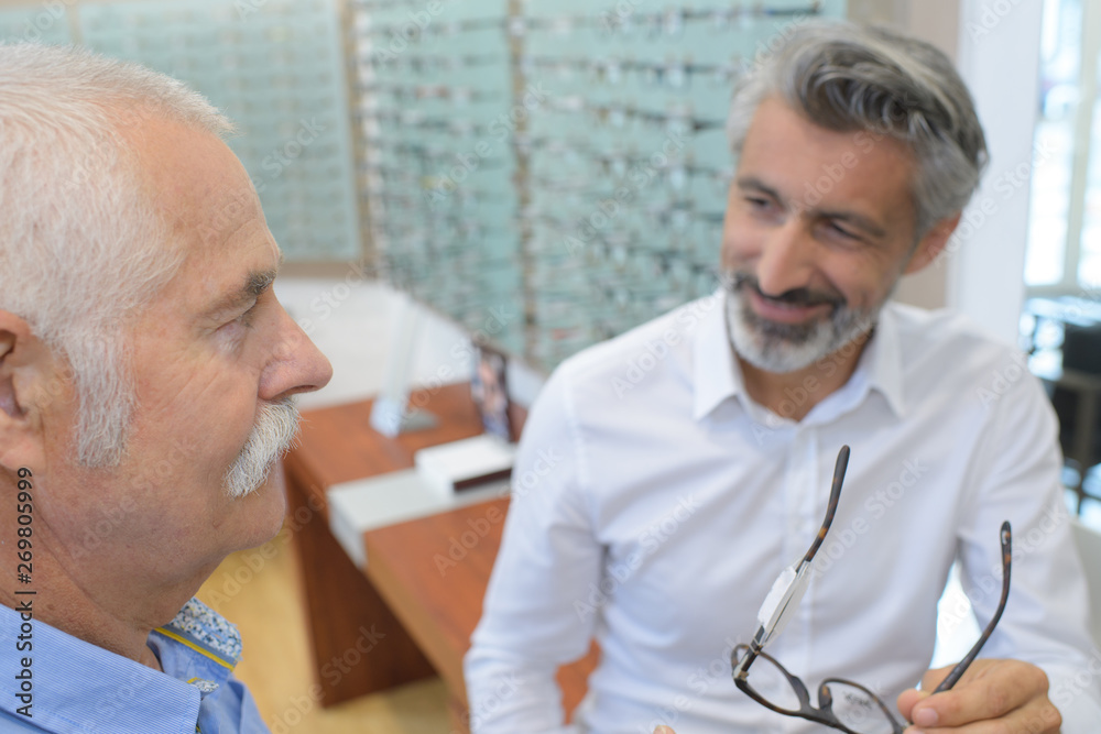 handsome optician showing glasses to senior man at optics store