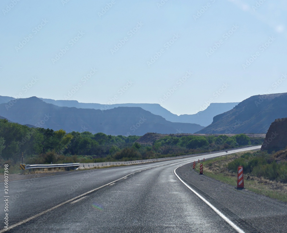 Wide shot of paved winding road to Zion National Park, with silhouettes of the mountains in varying hues of blue. Wide shot of paved winding road to Zion National Park, with silhouettes of the mountains in varying hues of blue.