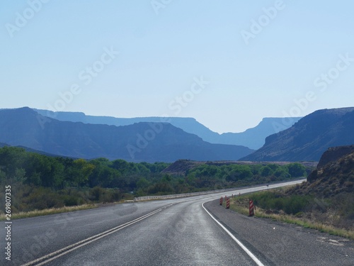 Paved winding road to Zion National Park, with silhouettes of the mountains in varying hues of blue.