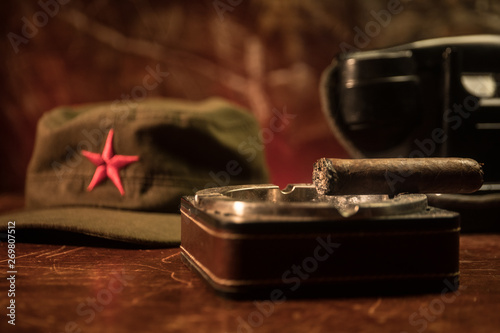 Close up of a Cuban cigar and ashtray on the wooden table. Communist dictator commander table in dark room. Army general`s work table concept. photo