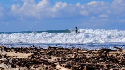 Large pile of winter driftwood piled on California beach with surfer riding a wave in the background