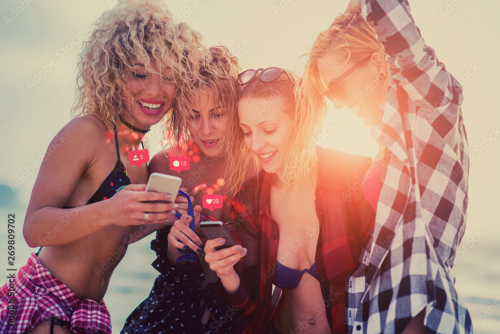 Four beautiful multicultural girlfriends standing on the beach at sunset and using smart phones for social media. Four beautiful multicultural girlfriends standing on the beach at sunset and using smart phones for social media.