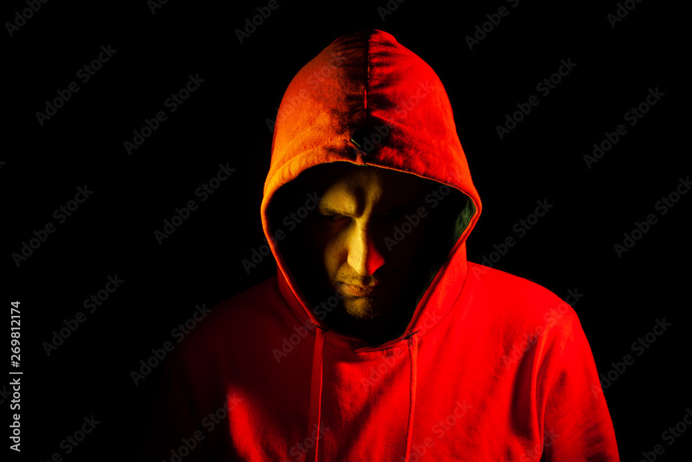 Close-up of the head of a man in an orange hood on the side of the side and looking down with a yellow backlight. Feeling before battle with a thoughtful look. Part of the face is hidden in the shadow