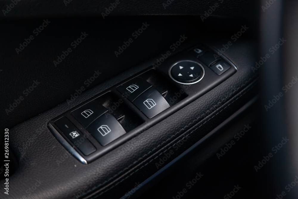 The control buttons for opening and closing windows of doors and electric controls and settings of mirrors on the door in black with leather upholstery in a luxury modern car.