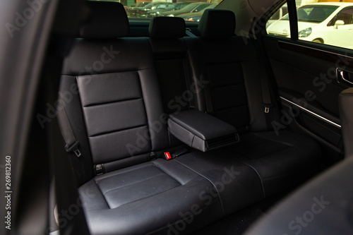 The rear seats of the car in the sedan body are black leather upholstered with the armrest folded down after dry cleaning and washing in a car repair shop. Auto service industry. © Aleksandr Kondratov