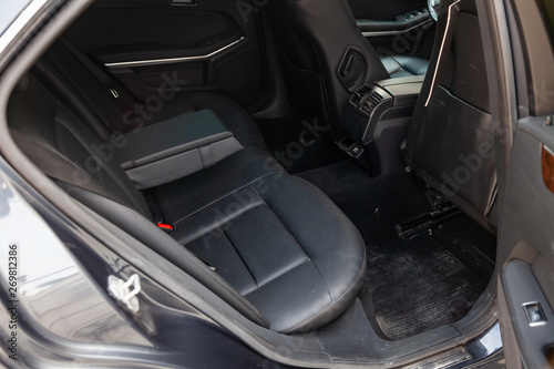 The rear seats of the car in the sedan body are black leather upholstered with the armrest folded down after dry cleaning and washing in a car repair shop. Auto service industry.