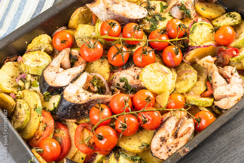Roast with vegetables and pieces of fish on a baking sheet - zucchini, cherry tomatoes on a branch, potatoes, onions, top view
