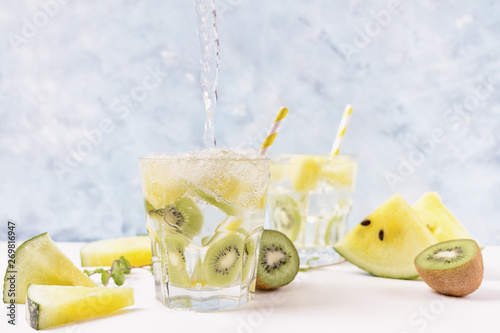 Cool soda water poring into yellow watermelon and kiwi lemonade with ingredients on bright blue background. Motion. Vegeterian food concept. Detox photo