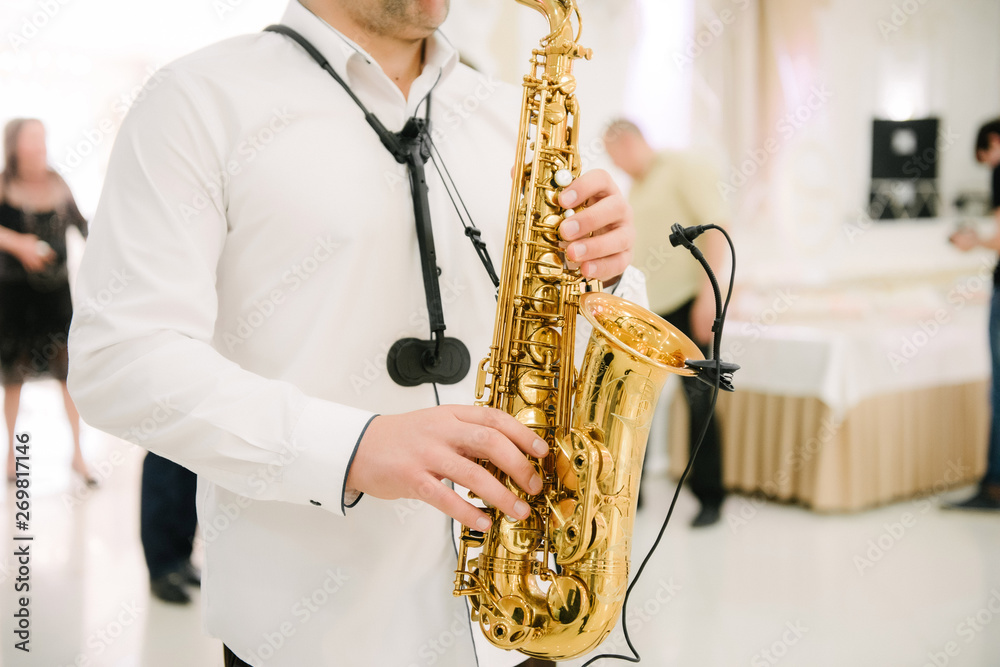 Naklejka premium The musician plays the saxophone indoors close-up. The saxophonist plays the saxophone at the event close-up.
