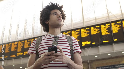 Man at train station checking timetables on mobile phone