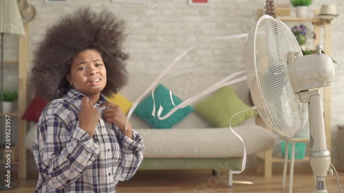 perplexed african woman with an afro hairstyle in front of the fan is saved from heat slow mo