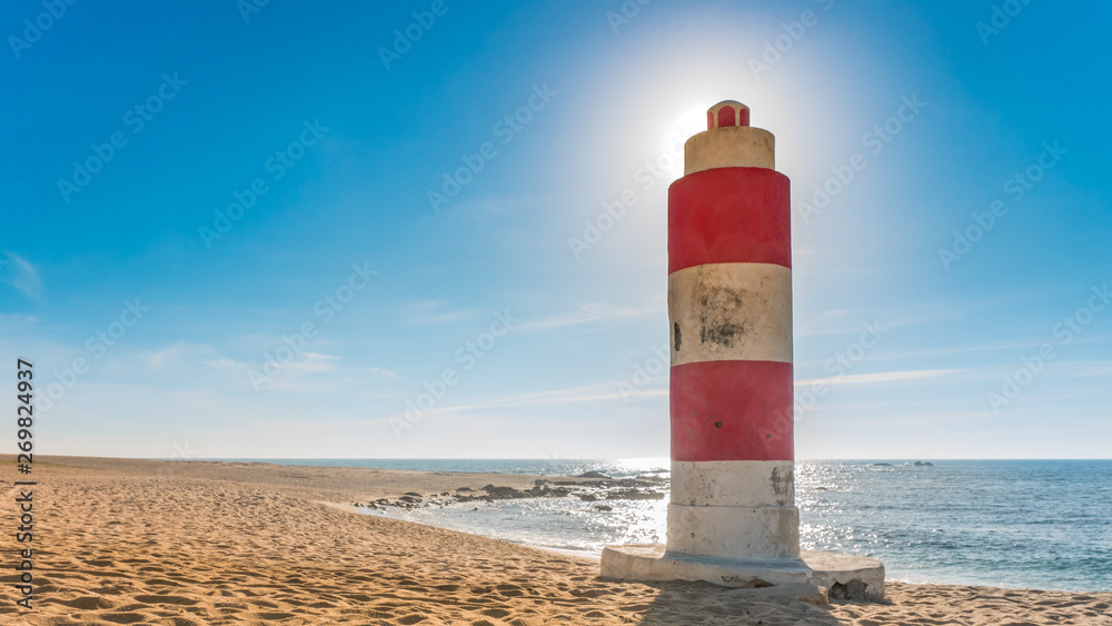 Fototapeta premium Lighthouse on beach in summer with sun producing halo effect