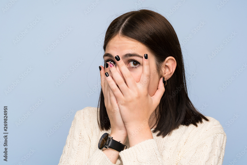 Young woman over isolated blue wall covering eyes and looking through fingers Young woman over isolated blue wall covering eyes and looking through fingers