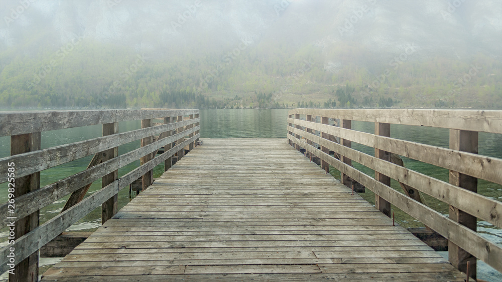 Fototapeta premium Pier on lake Bohinj. Fog over the water hides mountain at another bank of the lake.
