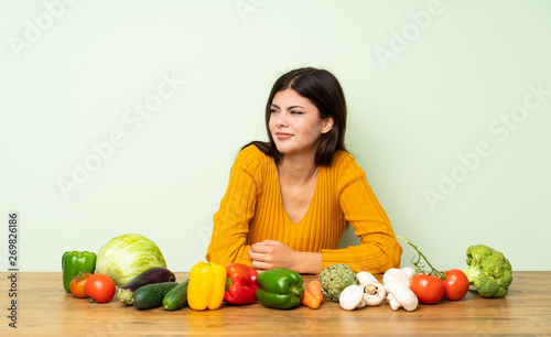 Teenager girl with many vegetables making doubts gesture looking side