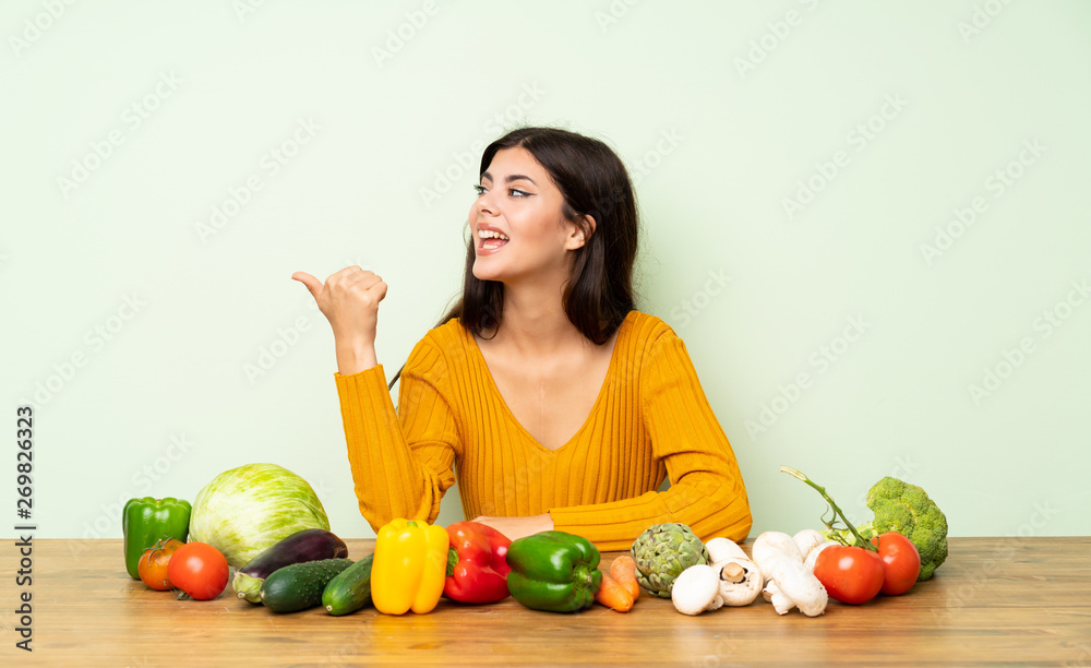 Teenager girl with many vegetables pointing to the side to present a product Teenager girl with many vegetables pointing to the side to present a product