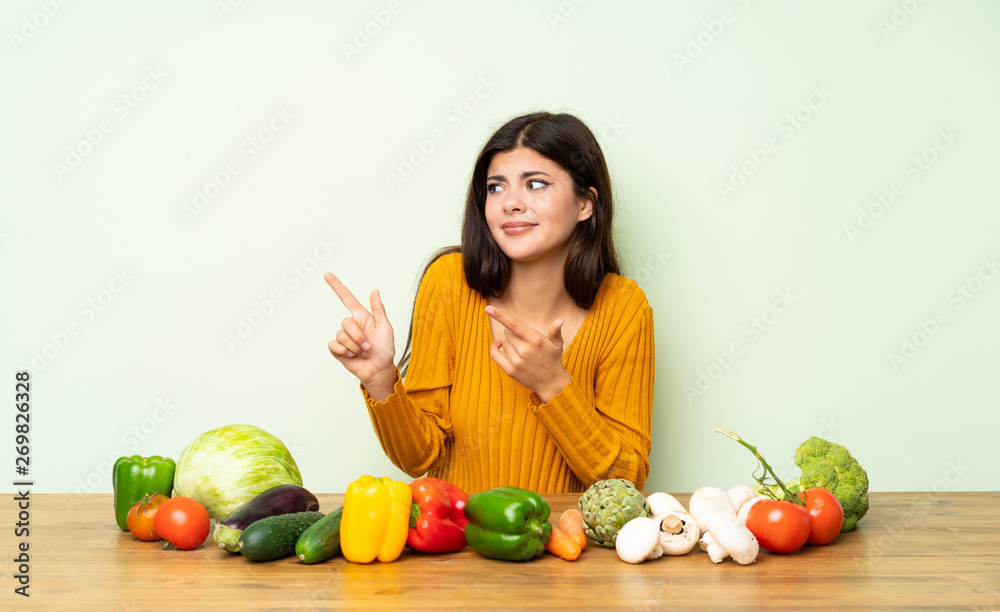 Teenager girl with many vegetables frightened and pointing to the side Teenager girl with many vegetables frightened and pointing to the side