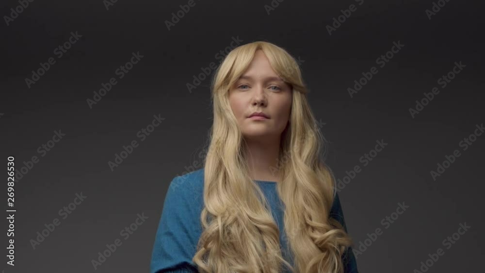 nordic blond model in studio with dramatic top light. Blonde long hair. Turns to the camera and watching to the camera, slightly smiling