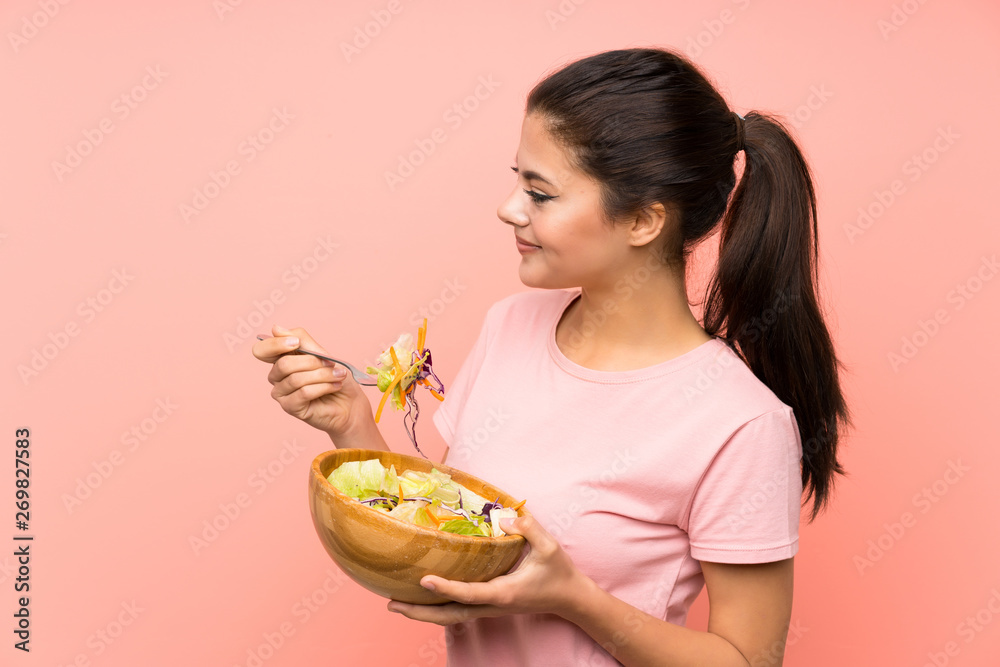 Teenager girl over isolated pink wall with salad Teenager girl over isolated pink wall with salad