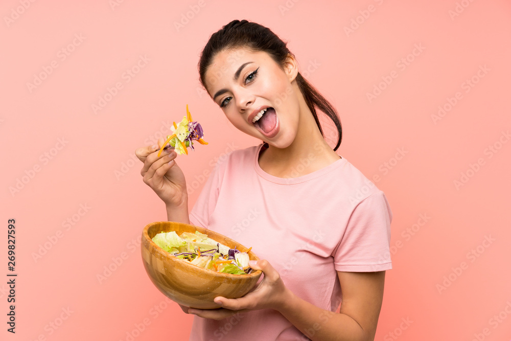 Happy Teenager girl  over isolated pink wall with salad