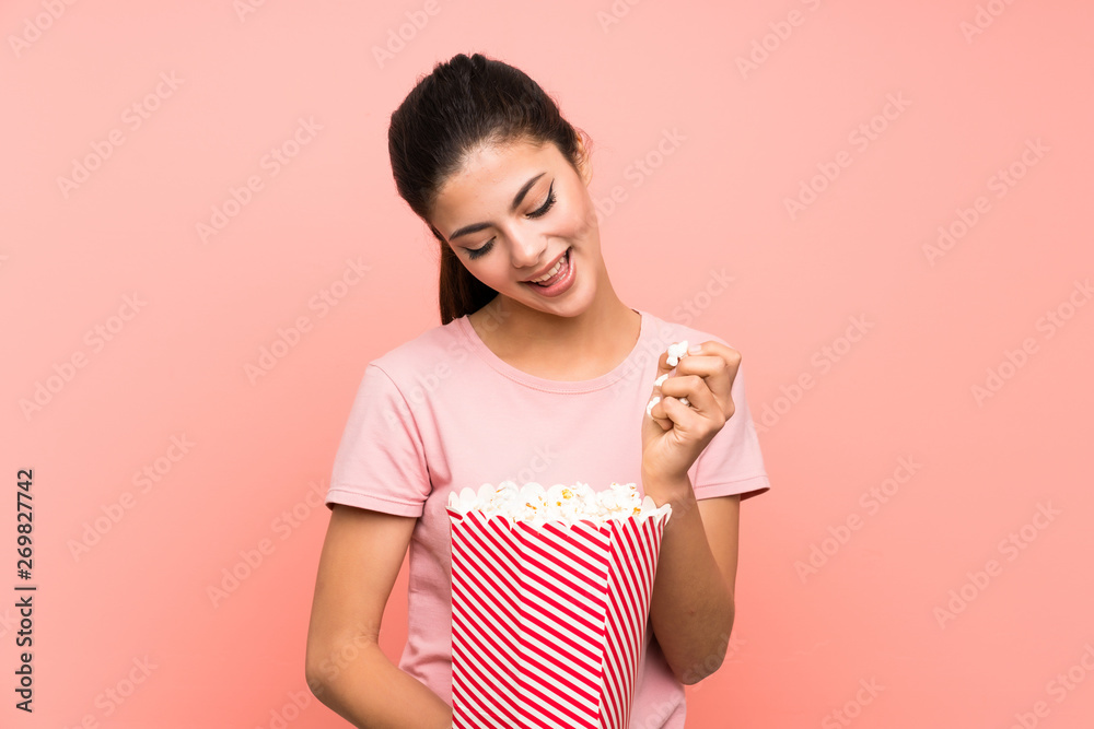 Teenager girl over isolated pink wall eating popcorns Teenager girl over isolated pink wall eating popcorns