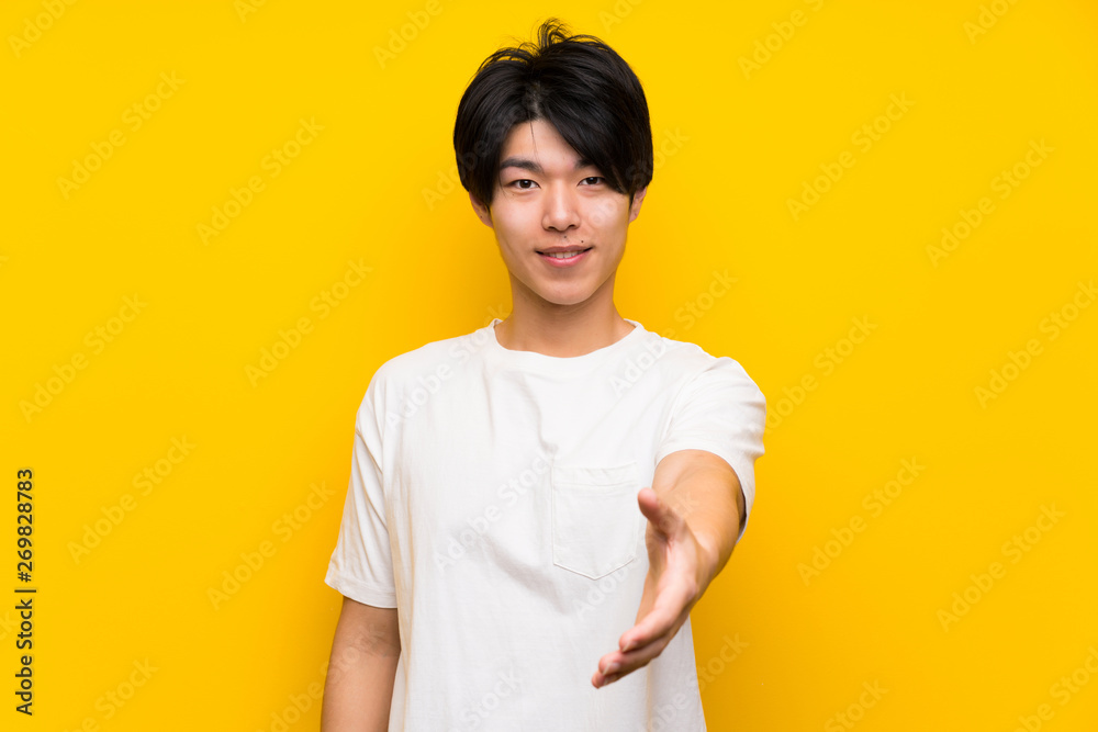 Asian man over isolated yellow wall shaking hands for closing a good deal Asian man over isolated yellow wall shaking hands for closing a good deal