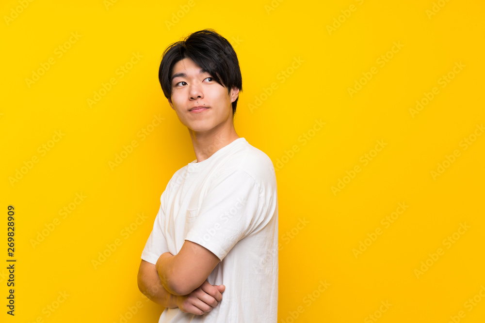 Asian man over isolated yellow wall with arms crossed and happy
