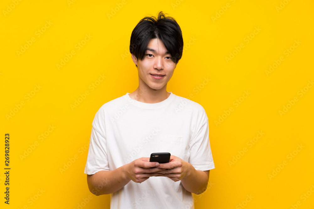 Asian man over isolated yellow wall sending a message with the mobile