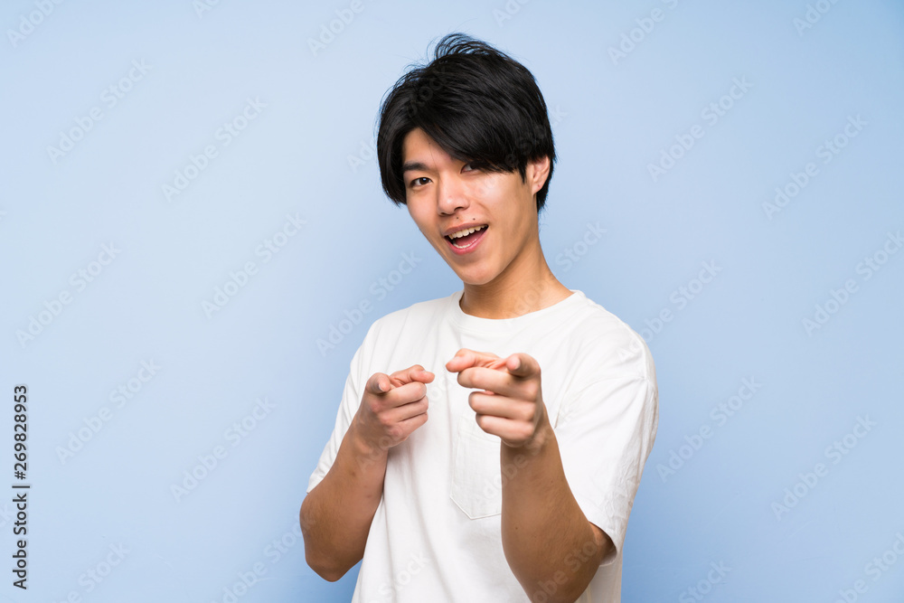 Asian man on isolated blue background points finger at you