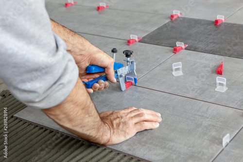 Ceramic Tiles. Tiler placing ceramic wall tile in position over adhesive with lash tile leveling system - Image