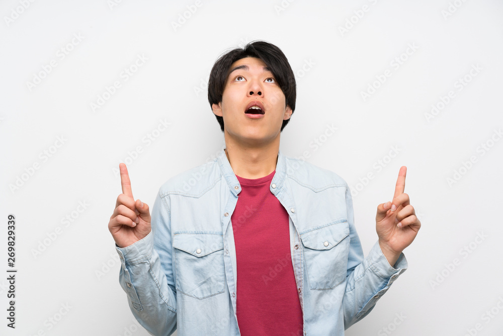 Asian man on isolated white background surprised and pointing up Asian man on isolated white background surprised and pointing up