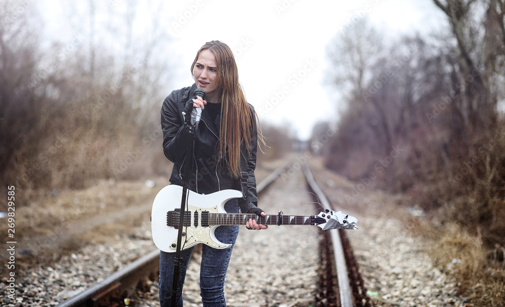 Beautiful young girl rocker with electric guitar. A rock musician girl in a leather jacket with a guitar sings. A rock band soloist plays the guitar and screams into the microphone.