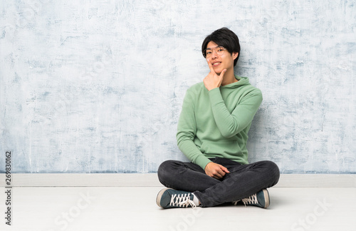 Asian man sitting on the floor with glasses and smiling