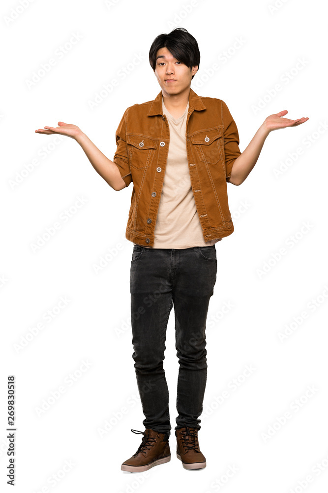 A full-length shot of a Asian man with brown jacket having doubts while raising hands over isolated white background