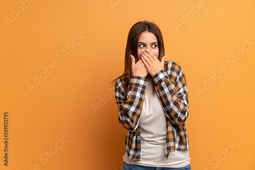 Young woman over brown wall covering mouth and looking to the side © luismolinero