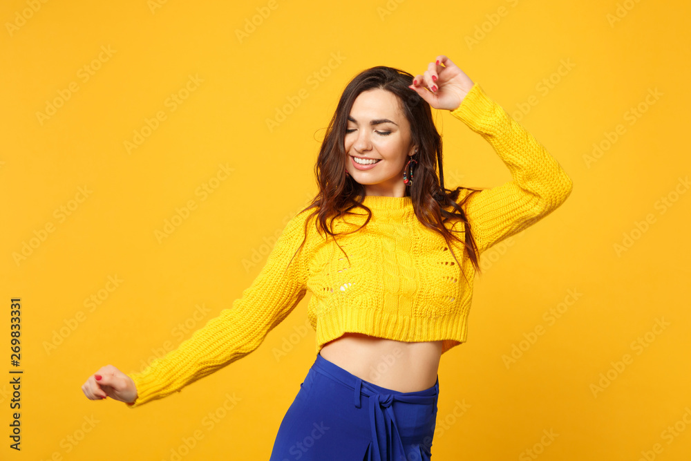 Portrait of pretty young woman in sweater, blue trousers keeping eyes closed rising spreading hands isolated on yellow orange background. People sincere emotions lifestyle concept. Mock up copy space. Portrait of pretty young woman in sweater, blue trousers keeping eyes closed rising spreading hands isolated on yellow orange background. People sincere emotions lifestyle concept. Mock up copy space.
