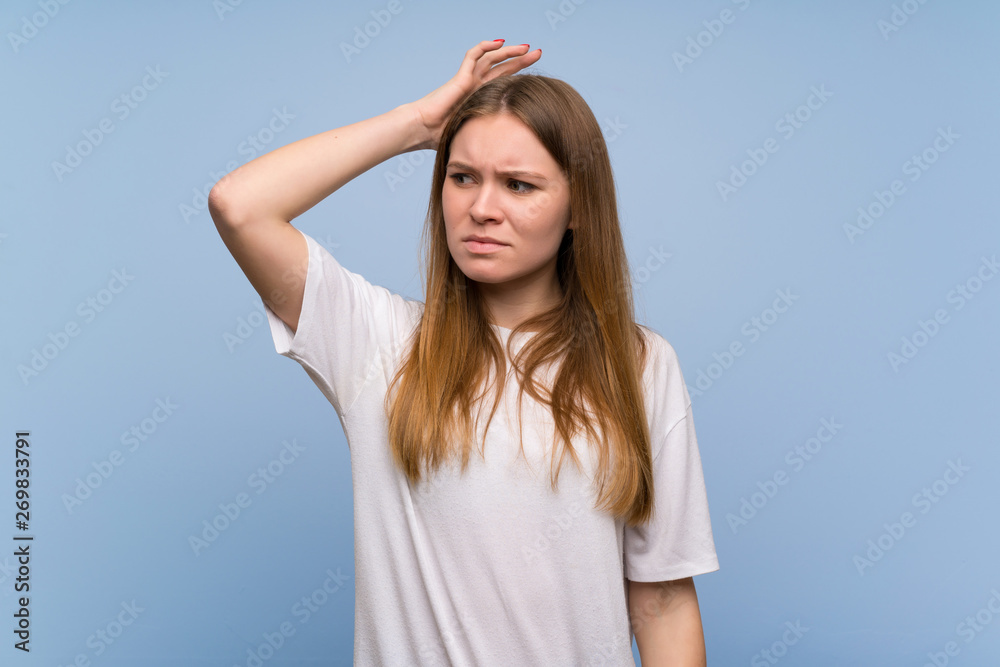 Young woman over blue wall having doubts while scratching head Young woman over blue wall having doubts while scratching head
