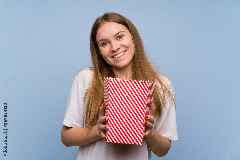 Young woman over blue wall eating popcorns Young woman over blue wall eating popcorns