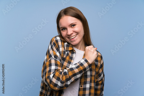 Young woman over blue wall celebrating a victory