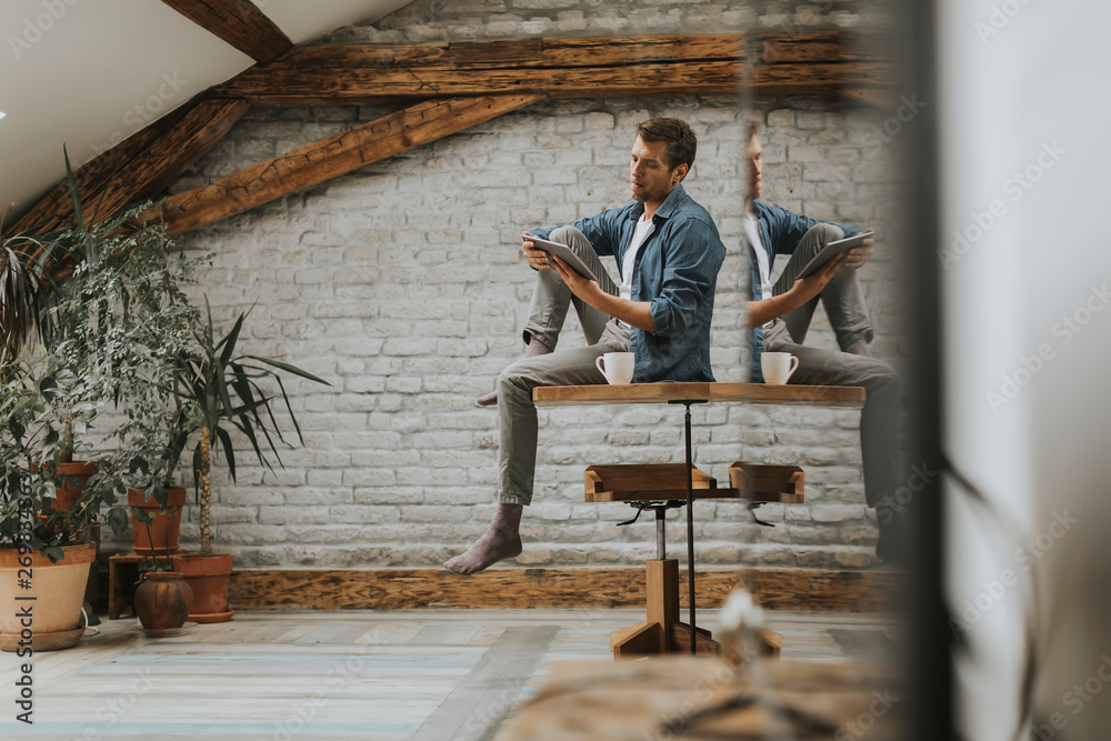Handsome young man using digital tablet while sitting in the rustic room Handsome young man using digital tablet while sitting in the rustic room