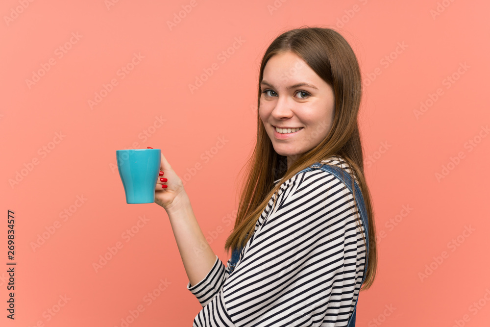Young woman with overalls over pink wall holding a hot cup of coffee Young woman with overalls over pink wall holding a hot cup of coffee