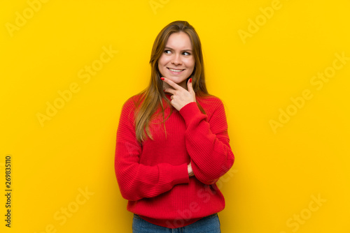 Young woman over yellow wall looking to the side © luismolinero